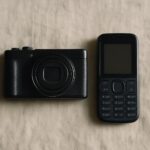 A compact digital camera beside a basic keypad phone, illustrating the choice of a dumb phone with a good camera